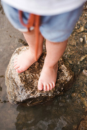 Nahaufnahme von Kinderfüßen, die auf einem Felsen in einem flachen Gewässer stehen