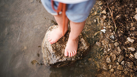 Nahaufnahme von Kinderfüßen, die auf einem Felsen in einem flachen Gewässer stehen