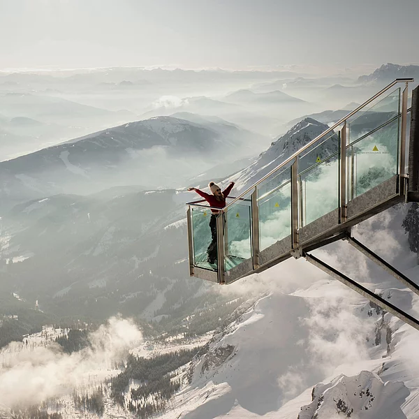Frau auf einer verglasten Aussichtsplattform mit Blick auf die Berglandschaft in Schladming