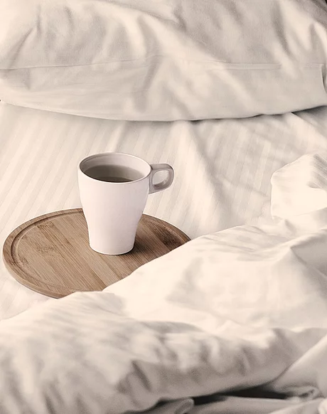 Bett mit weißer Bettwäsche und einem Tablett mit einer Tasse Tee