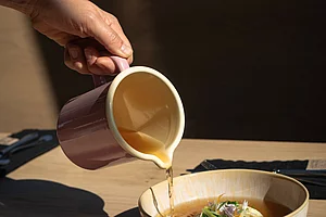 Klare Suppe wird aus Krug über feine Einlage in Keramikschale gegossen im Restaurant in Schladming