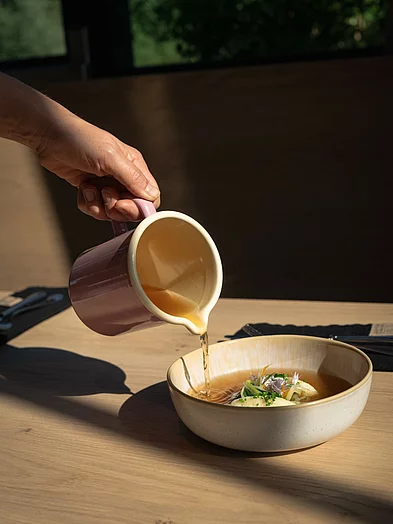 Gasthaus Klare Suppe wird aus Krug über feine Einlage in Keramikschale gegossen im Restaurant in Schladming