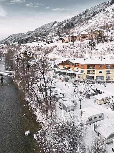 Kontakt & Anreise Luftaufnahme des Haus Zirngast in Schladming, umgeben von verschneiten Bergen und einem Fluss im Winter